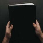 7 pecados capitais na Biblia: maos segurando a Biblia preta representando o peso do pecado e a busca por redencao