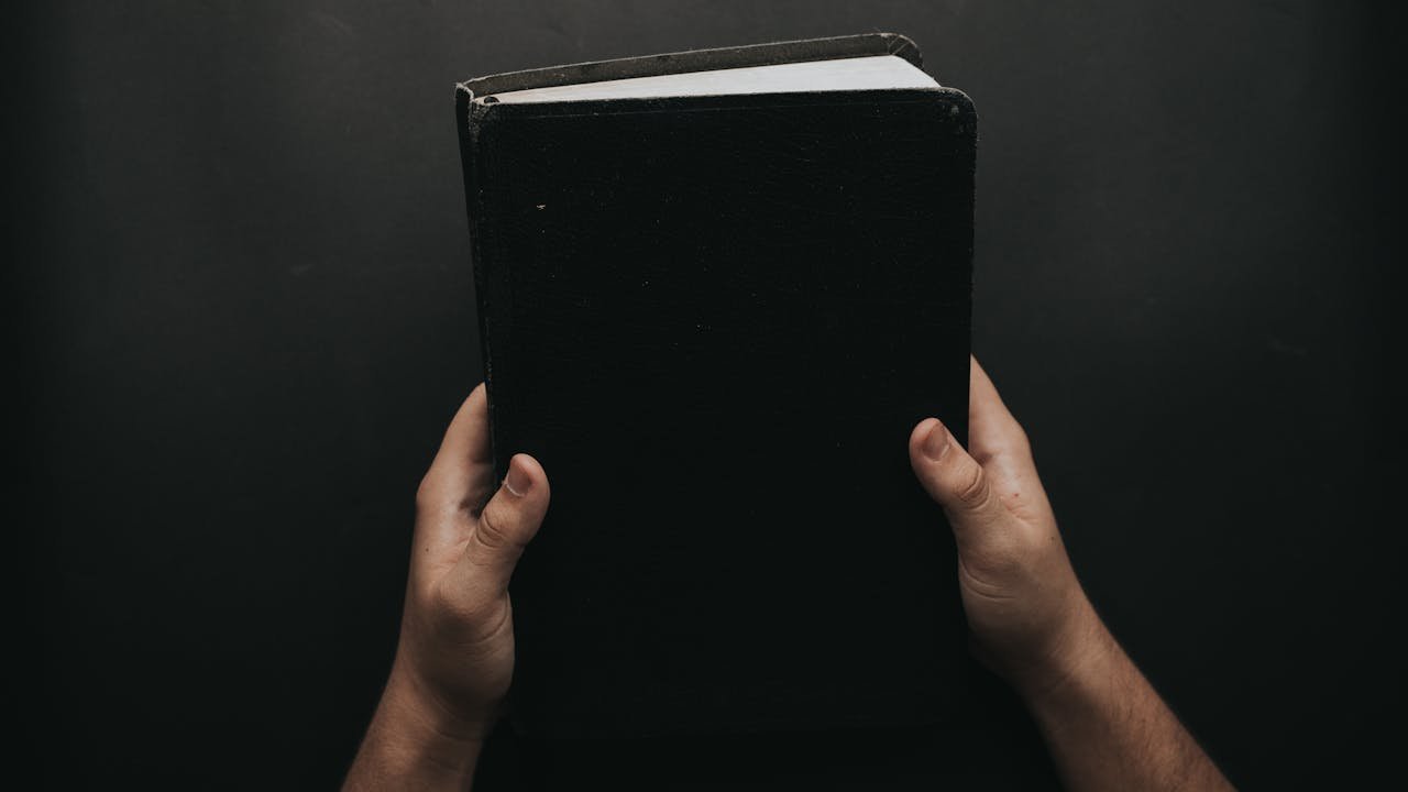 7 pecados capitais na Biblia: maos segurando a Biblia preta representando o peso do pecado e a busca por redencao